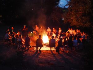 die Teilnehmenden des inklusiven Zeltlagers sitzen in einem Kreis um das Lagerfeuer bei Dunkelheit