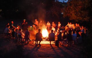 die Teilnehmenden des inklusiven Zeltlagers sitzen in einem Kreis um das Lagerfeuer bei Dunkelheit