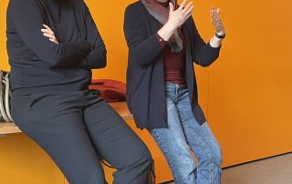 Die Bundestagsabgeordneten Dr. Manuela Rottmann und Sabine Dittmar vor einer orangenen Wand im Gespräch
