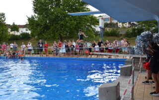 Ein Mädchen springt von einem Sprungturm vor Zuschauern ins Wasser