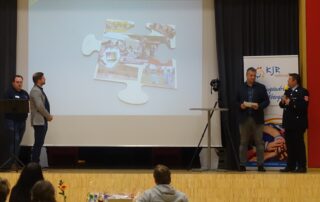 Die Jugendfeuerwehr stellt auf der Bühne ihr Puzzleteil im Rahmen der 75 Jahrfeier des Kreisjugendrings Haßberge vor. Auf der Leinwand ist das Puzzleteil zu erkennen.