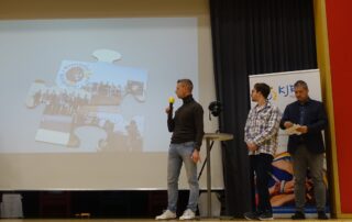 Die bayerische Schützenjugend stellt auf der Bühne ihr Puzzleteil im Rahmen der 75 Jahrfeier des Kreisjugendrings Haßberge vor. Auf der Leinwand ist das Puzzleteil zu erkennen.