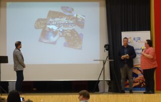 Die THW Jugend stellt auf der Bühne ihr Puzzleteil im Rahmen der 75 Jahrfeier des Kreisjugendrings Haßberge vor. Auf der Leinwand ist das Puzzleteil zu erkennen.