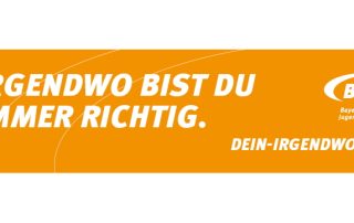 "Irgendwo bist du immer richtig" auf einem orangenen Banner des bayerischen Jugendrings