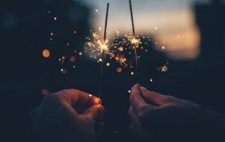 Zwei brennende Wunderkerzen werden von zwei Händen in der Dunkelheit gehalten