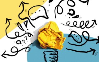 Eine Glühbirne aus geknülltem Papier vor zwischen vielen Zeichen, die Brainstorming darstellen