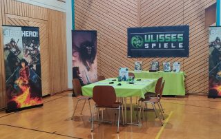 Der Stand des Spieleverlags Ulisses bei den Spieletagen 2023 mit einem Tisch mit grüner Decke