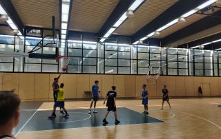 Jugendliche in einer Halle beim Basketballtraining werfen auf den Korb