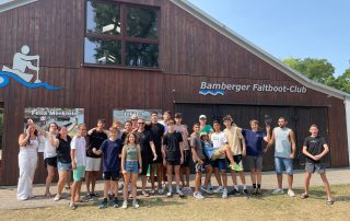 Die Teilnehmenden der Jugendbegegnung stehen vor einer Halle des Bamberger Faltboot-Clubs