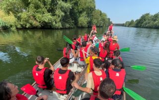 Die Teilnehmenden der Jugendbegegnung sitzen in Schwimmwesten auf einem Boot und rudern