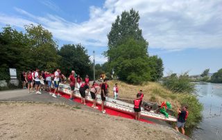 Die Teilnehmenden der Jugendbegegnung lassen gemeinsam das Boot zu Wasser