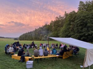 Jugendliche sitzen am Lagerfeuer beim Zeltlager in Reutersbrunn vor einem lila Himmel
