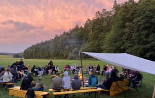 Jugendliche sitzen am Lagerfeuer beim Zeltlager in Reutersbrunn vor einem lila Himmel