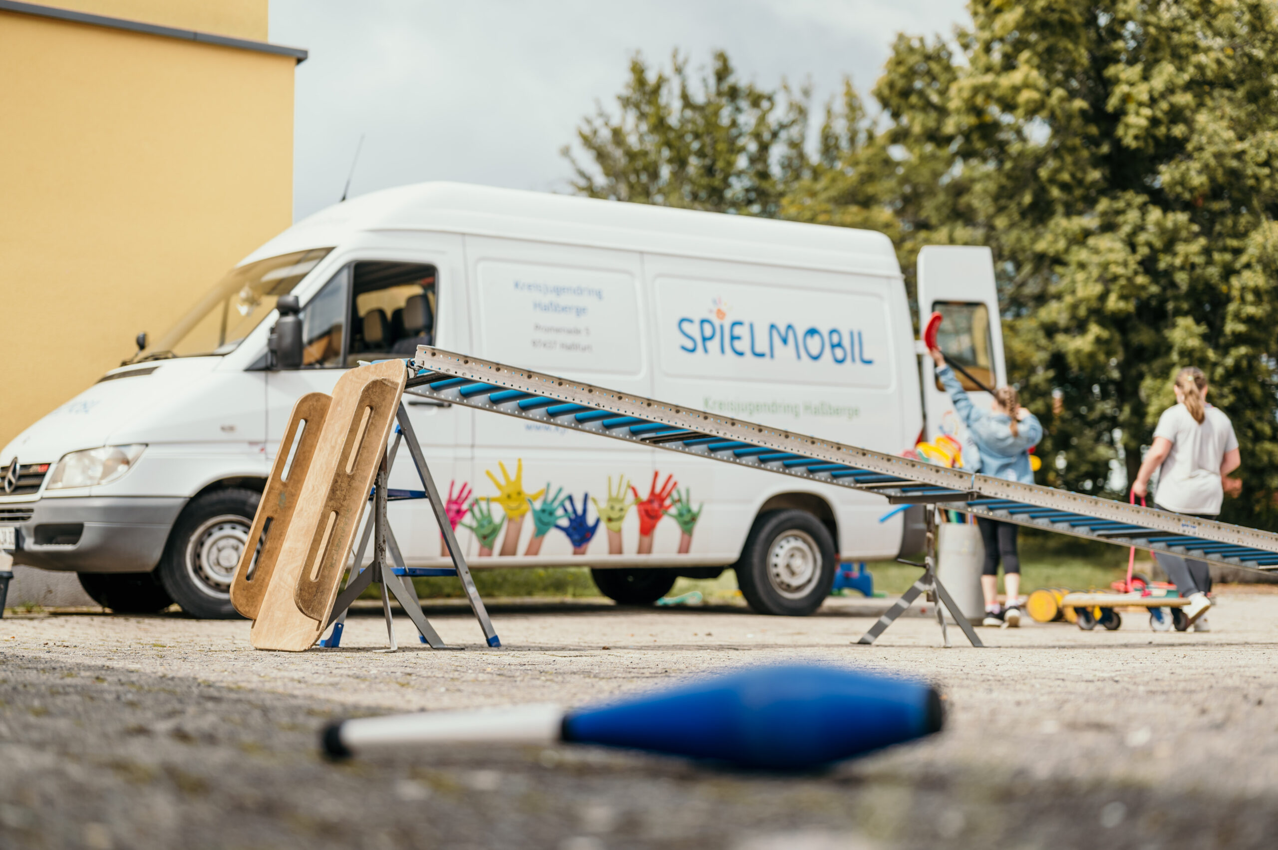 Rollenrutsche aufgebaut und im Einsatz beim Spielmobil von der Seite. Dahinter ein Schlitten