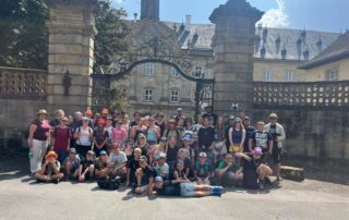 Rund 45 Kinder und 20 Teammitglieder stehen vor dem großen Tor vom Wildpark Schloss Tambach für ein Gruppenfoto zusammen.