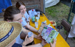 Drei Betreuer schauen sich die verschiedenen zur Auswahl stehenden Milchkartons beim Milchtasting im Rahmen des Lagerspiels am Zeltplatz an.