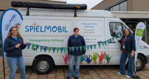 Eva Pfeil, Tamara Gräb und Susanne Makowski stehen vor dem Spielmobil und kündigen das 35. Spielmoibljubiläum im Jahr 2026 an.